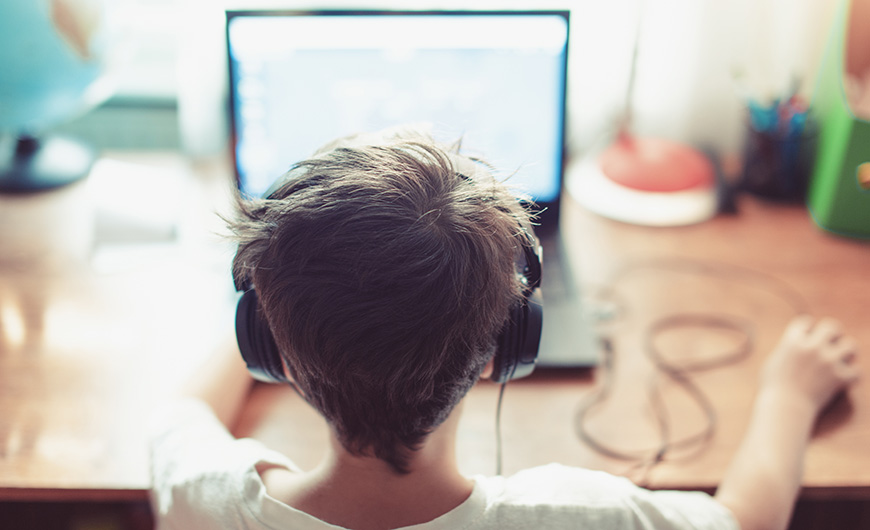 Young boy wearing headphones and playing on his laptop