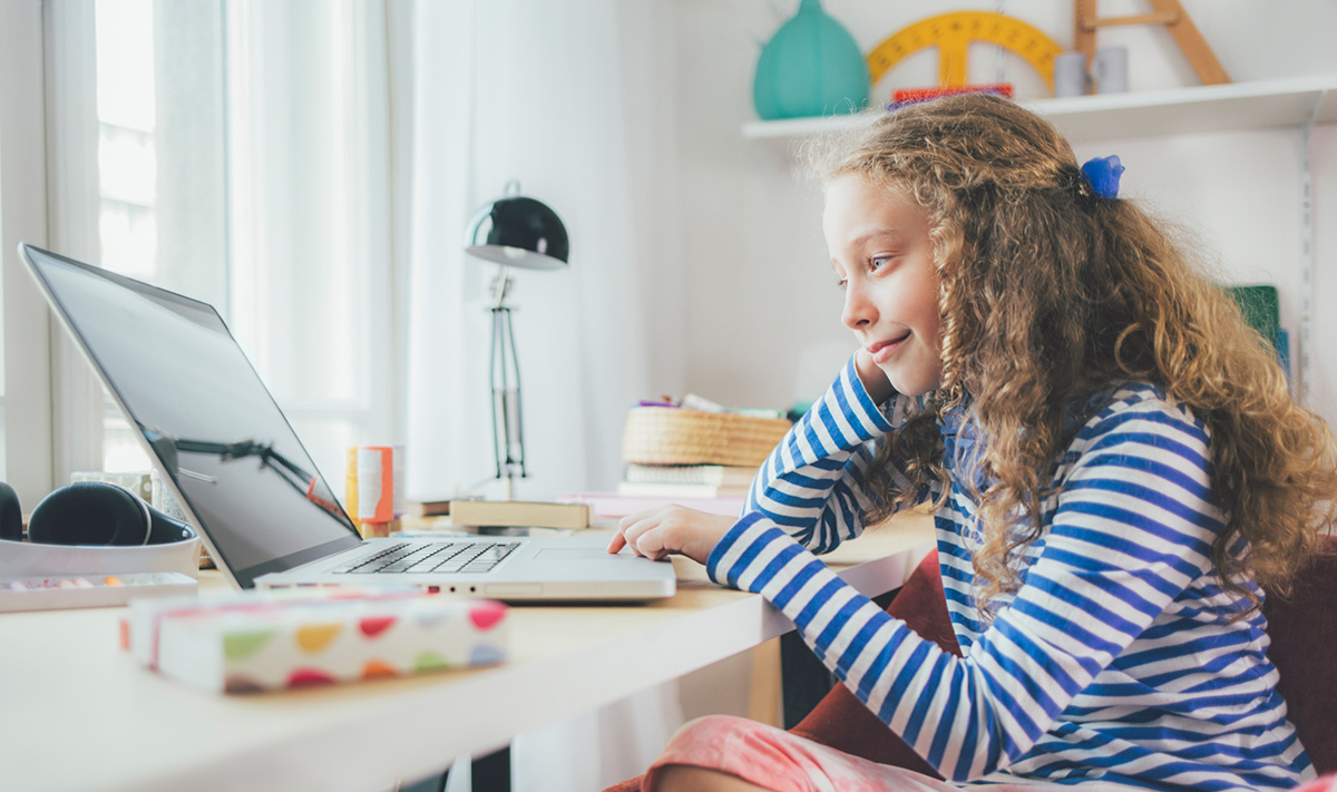 A young girl sits at her desk and works on her laptop